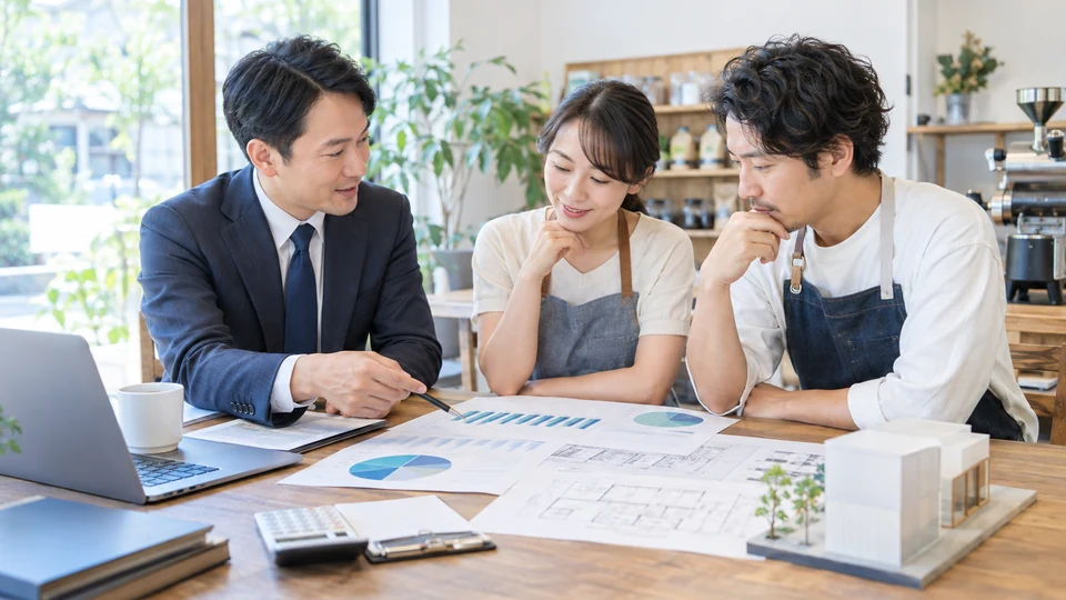 小規模事業者と支援者が、無文字の資金計画、キャッシュフロー資料、設備投資の見通しを机上で整理する場面。必要資金と事業の見通しを考える場面として表現する。